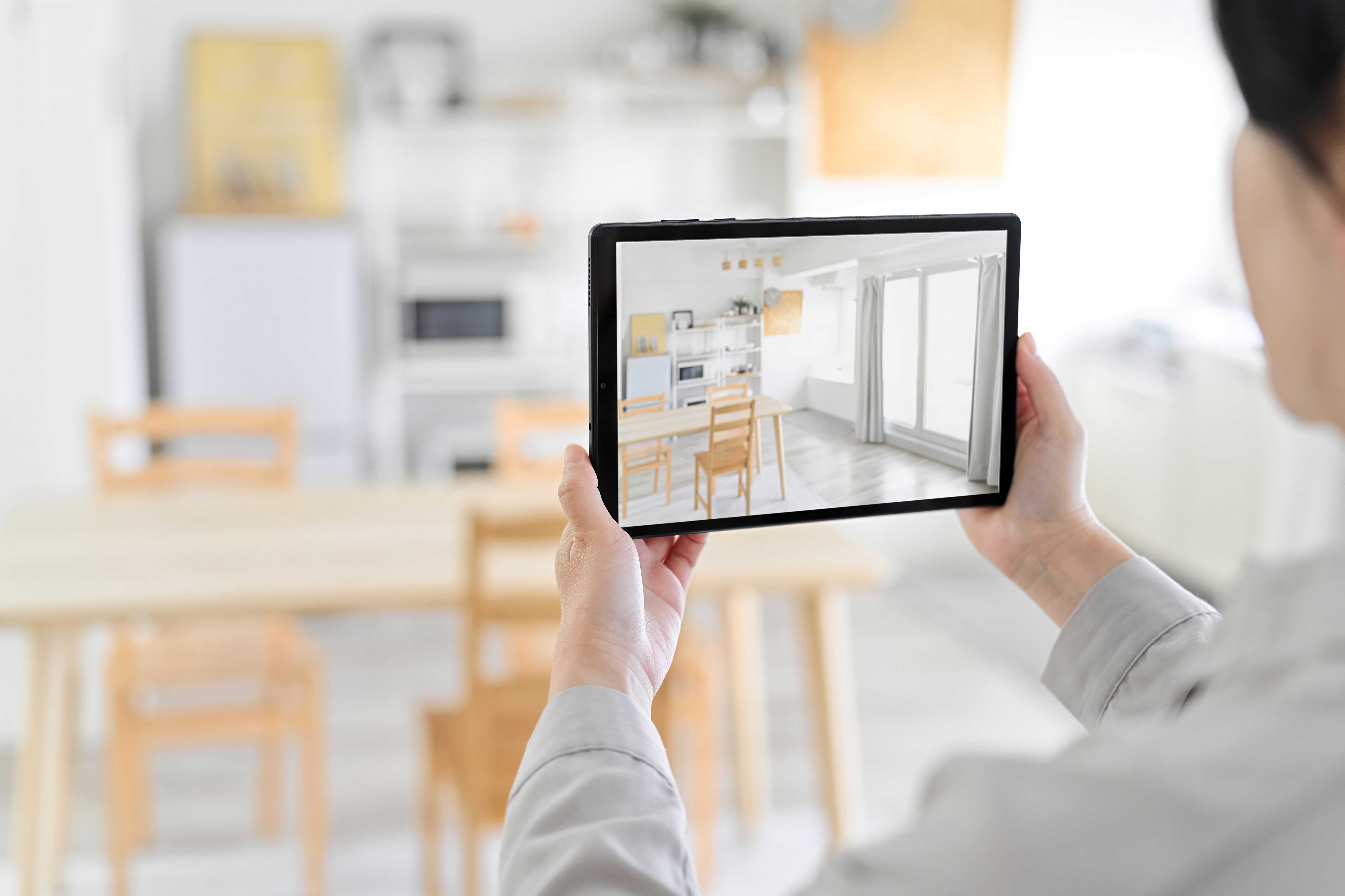 A woman holds a tablet to film her kitchen for a virtual tour. 