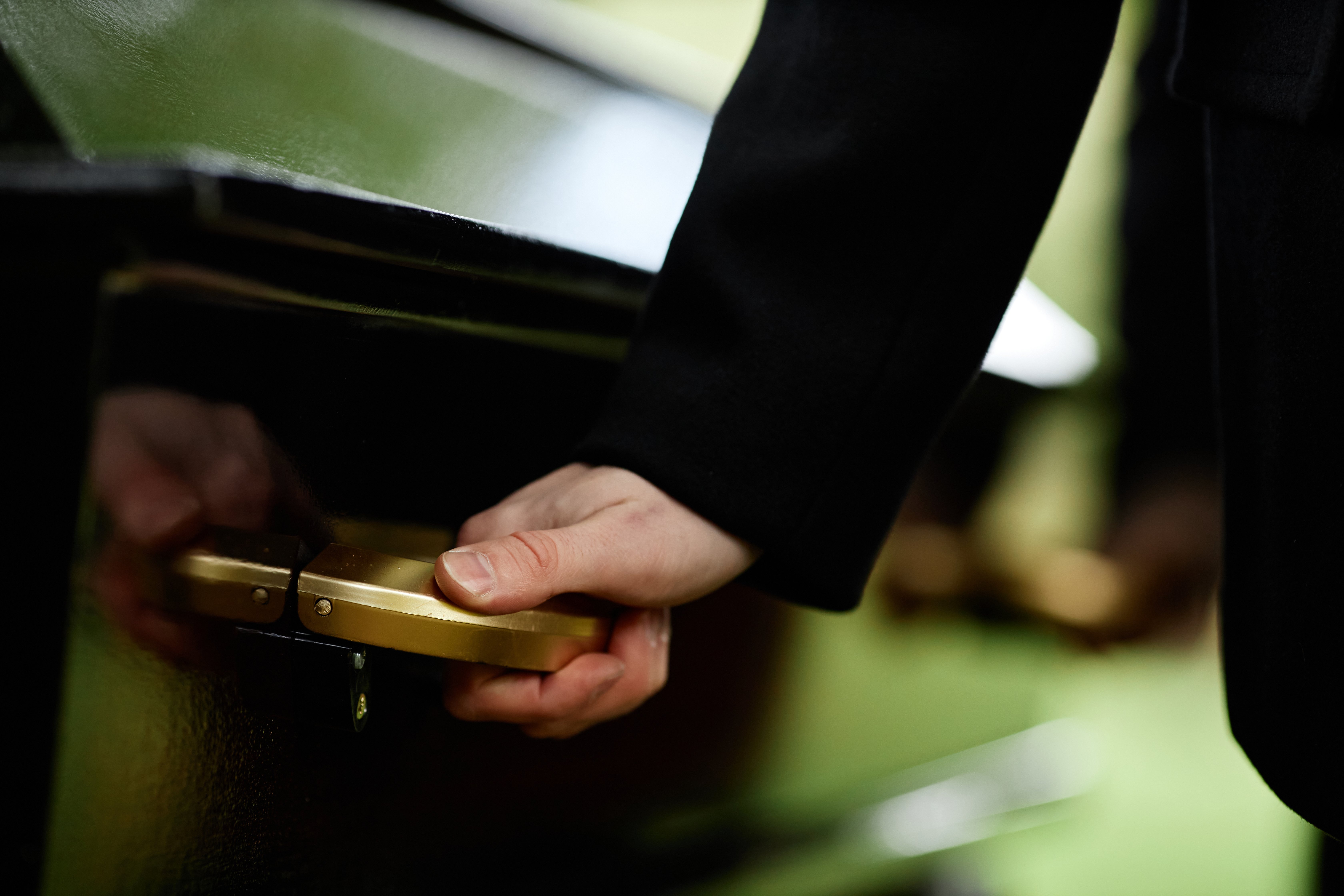 A hand holds the handle of a coffin