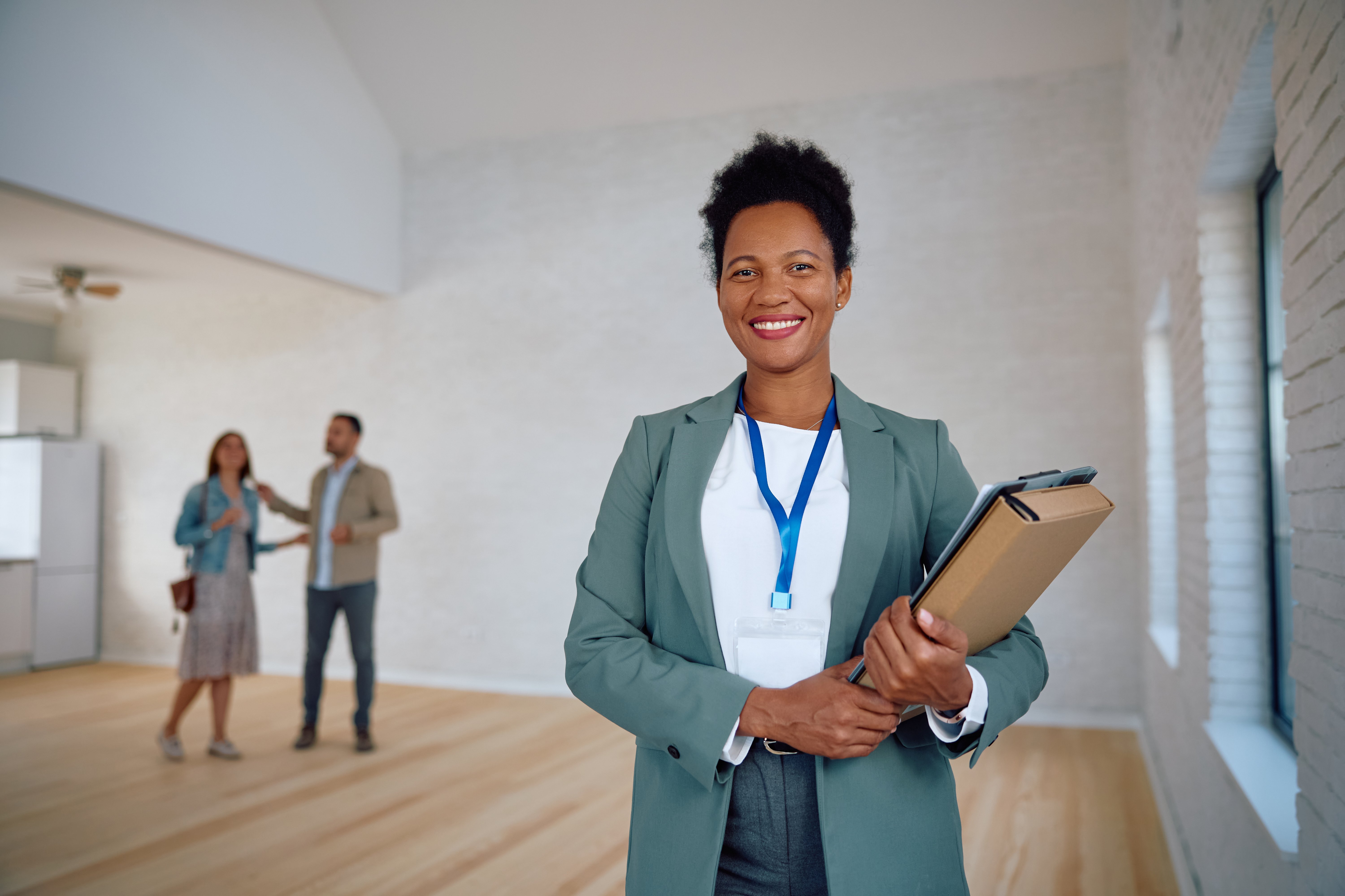 A new construction realtor holding documents with her two clients, a man and a woman, behind her.